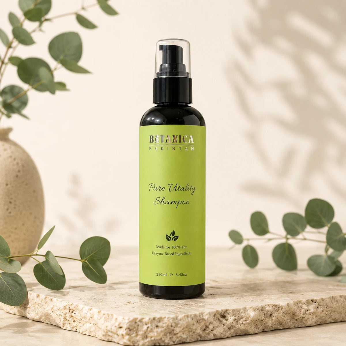 Botanica Parisin Pure Vitality Shampoo in a black bottle with a bright green label, styled on a stone slab with eucalyptus branches.