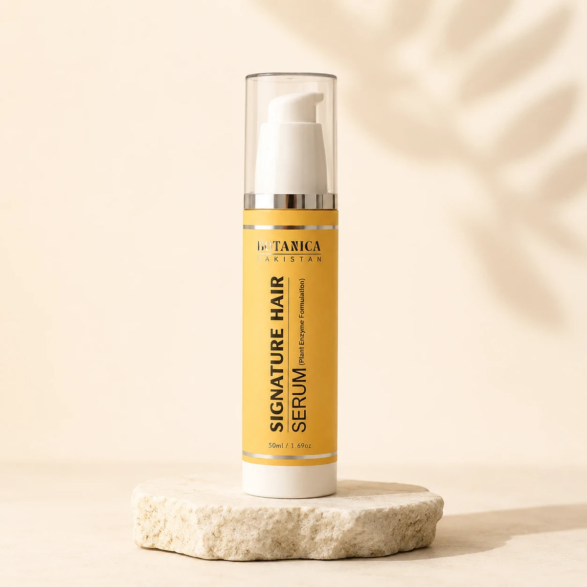 A bottle of BOTANICA Signature Hair Serum stands on a small stone slab against a warm beige background with soft leaf shadows. The bottle has a yellow label, a white pump, and a clear cap.