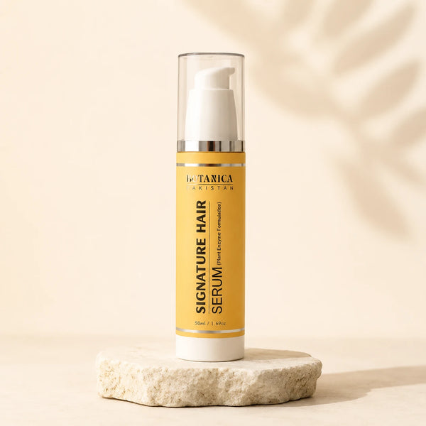 A bottle of BOTANICA Signature Hair Serum stands on a small stone slab against a warm beige background with soft leaf shadows. The bottle has a yellow label, a white pump, and a clear cap.